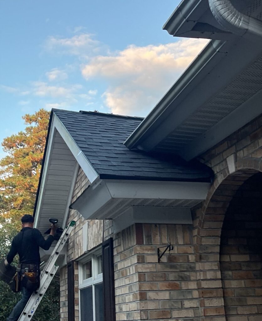 Palmetto roofer on a ladder working on gutter and fascia detail beneath a gable at dusk