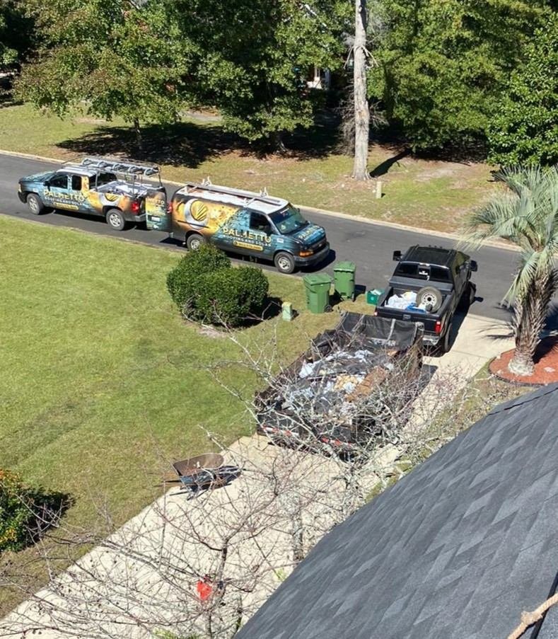 Palmetto Roofing and Solar branded truck and van parked on a residential street beside a dump trailer