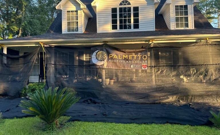 Palmetto Roofing and Solar banner hung across the front of a two-story home screened for a roof replacement