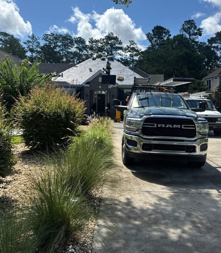 Palmetto Roofing truck in a driveway with a crew member working on the dried-in roof behind