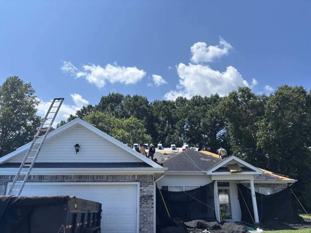 Palmetto Roofing crew replacing a shingle roof on a brick and vinyl home with the property screened off below