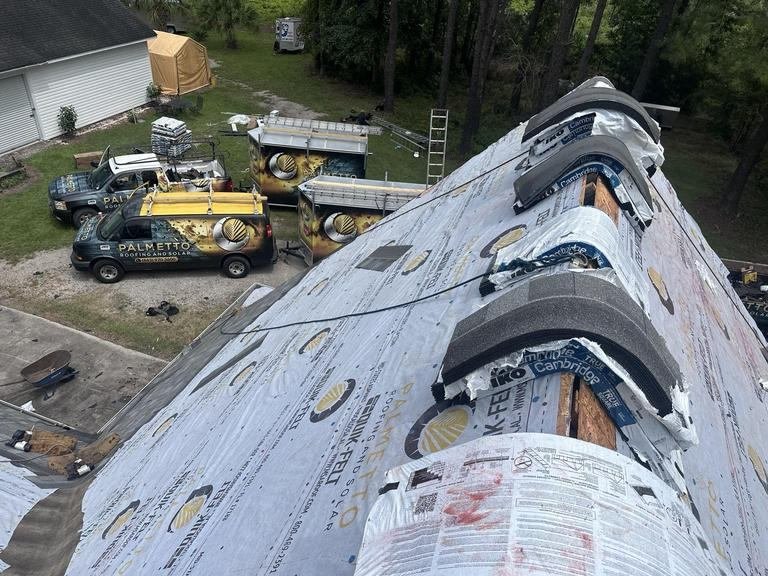Aerial view of a roof being replaced with Palmetto Roofing van and trailers parked in the driveway