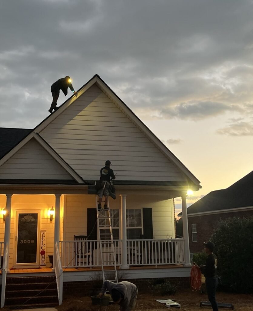Palmetto Roofing crew working on a roof after dark, lit by headlamps and work lights